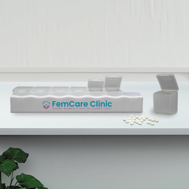 A white weekly pill box with multiple compartments, some open, alongside white pills and a plant. It has a logo.