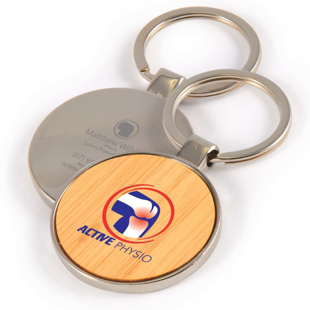 A round keytag with a bamboo front and a silver back, featuring a logo and keyring attachment.