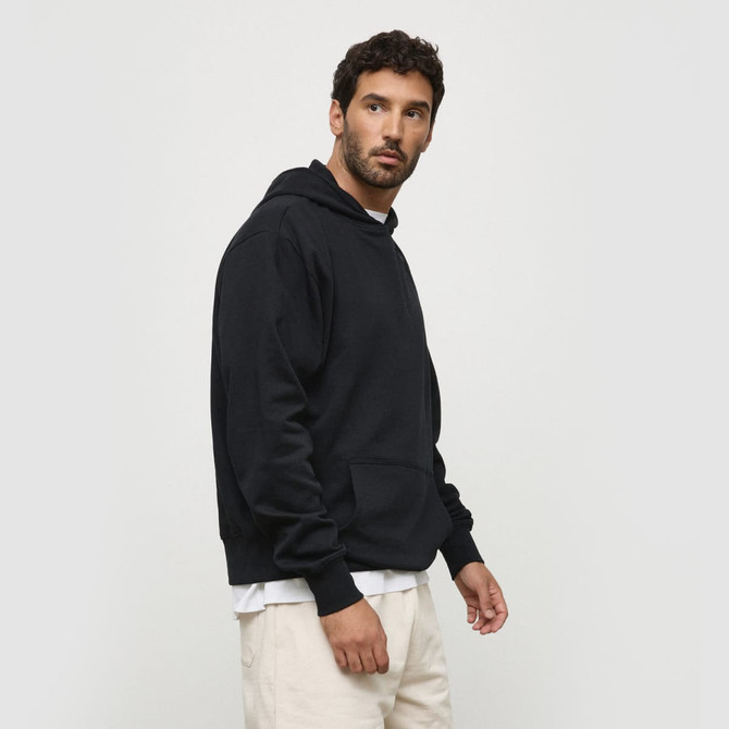 A black hoodie with a front pocket and a hood, displayed on a model standing sideways. Includes a logo.
