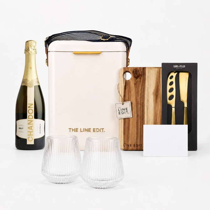 A champagne bottle, insulated bag, wooden chopping board, knife set, two glasses, and a blank card. The colours are neutral and earthy.
