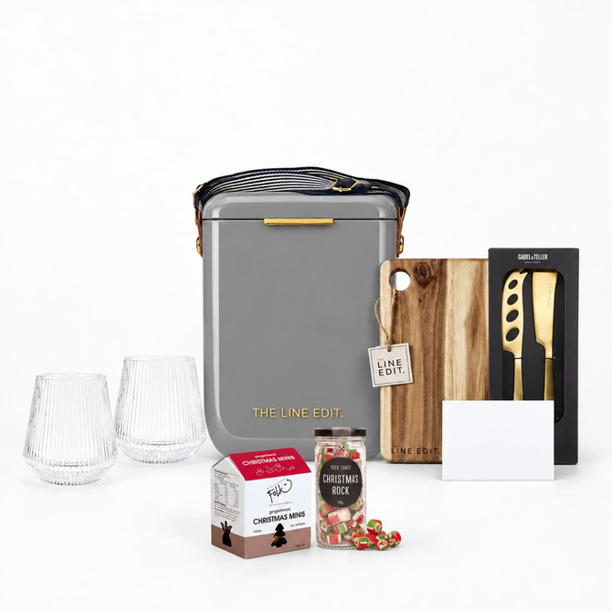A grey insulated bag, two clear glasses, a wooden cheese knife, a gift box, and festive snacks.