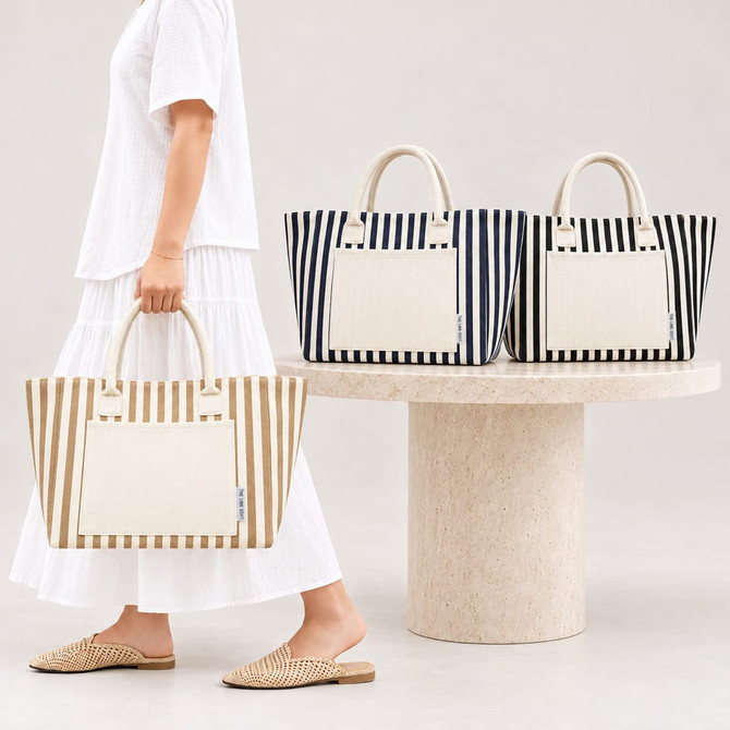 A striped tote bag in beige and cream, with additional navy and white options, displayed on a stone table.