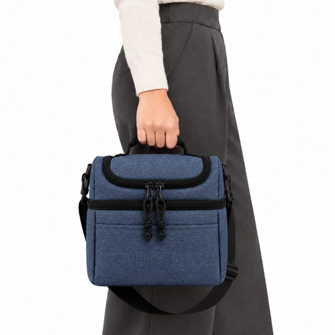 A blue cooler bag is being held by a person wearing a light sweater and grey pants. The bag features a logo.