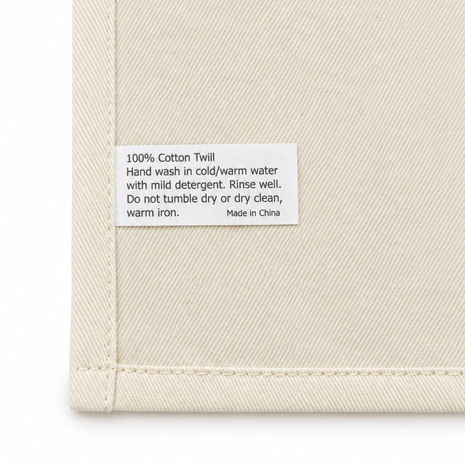 A cream cotton tea towel featuring a care label with washing instructions and a brand logo.