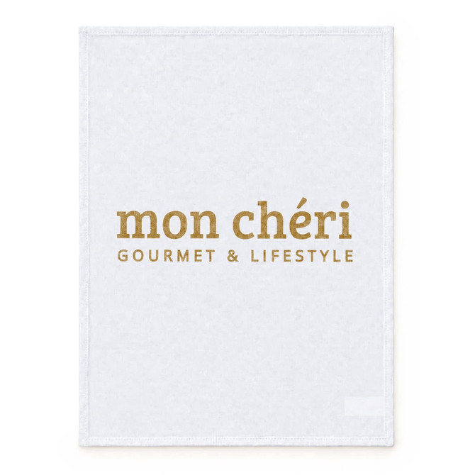A large, white cotton tea towel featuring gold text and a logo.