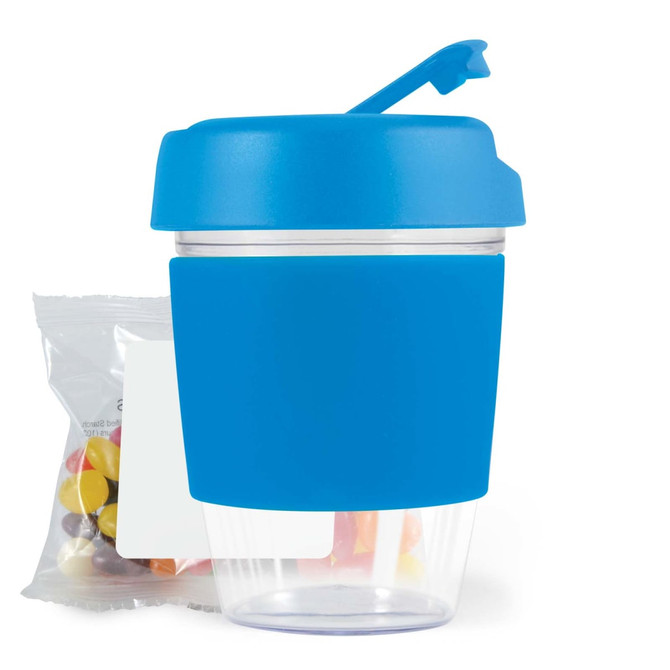 A reusable coffee cup in blue with a clear bottom and silicone sleeve, accompanied by a pack of jelly beans.