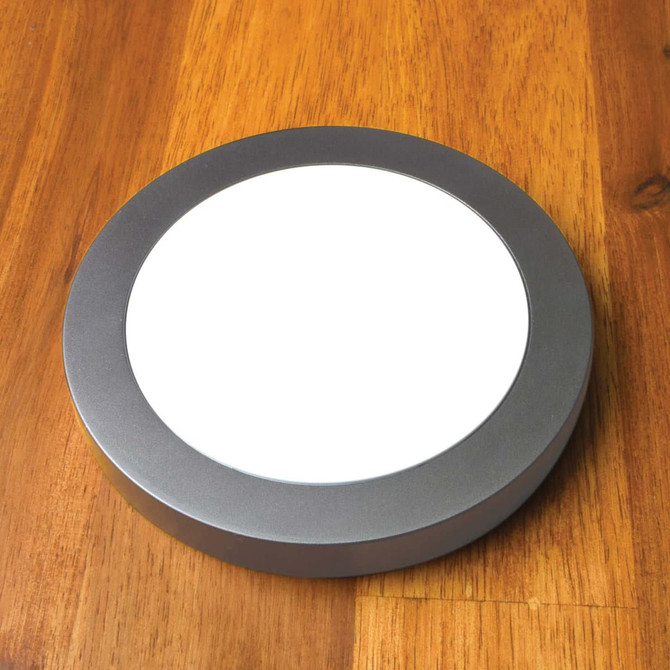 A round, silver wireless charger with a smooth, white charging surface, placed on a wooden surface.