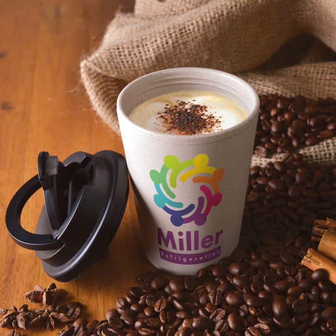 A reusable coffee cup in white with a black lid, surrounded by coffee beans and cinnamon. It features a colorful logo.