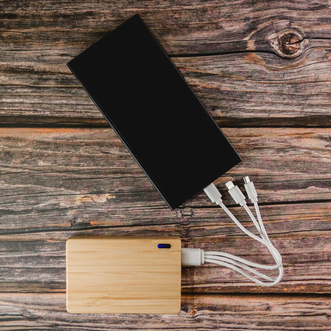 A bamboo power bank with multiple charging cables, alongside a larger black device, on a wooden surface.