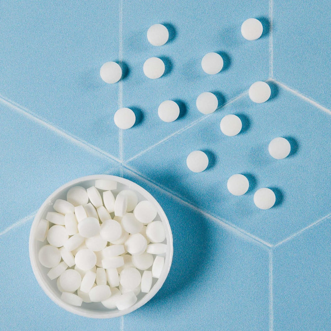A white bowl filled with round white mints, with several mints scattered around on a blue surface.