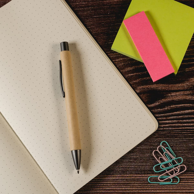A beige pen on a dotted notebook, surrounded by colourful sticky notes and paper clips.