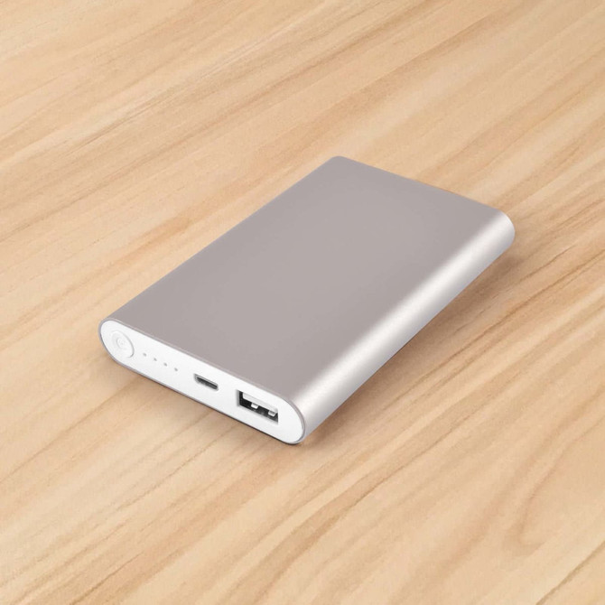 A silver power bank with a USB port on a wooden surface, featuring a sleek, minimal design and a logo.