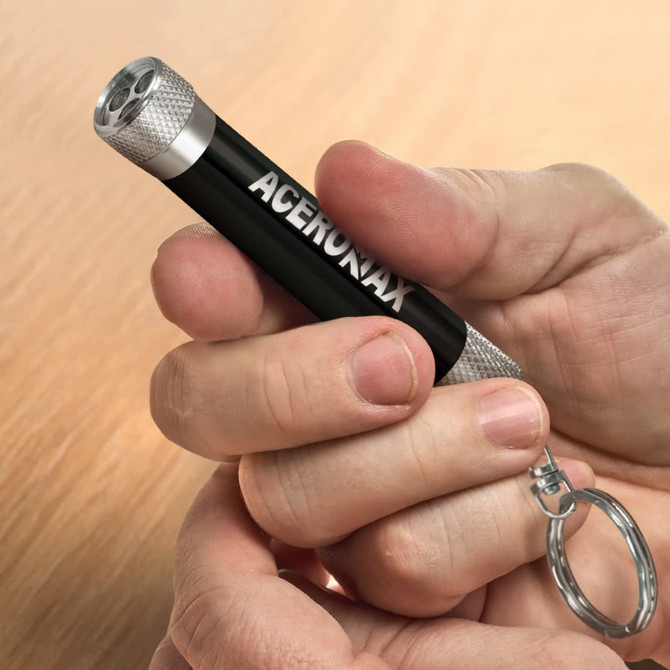 A key ring flashlight in black and silver, held in a hand, featuring a logo.