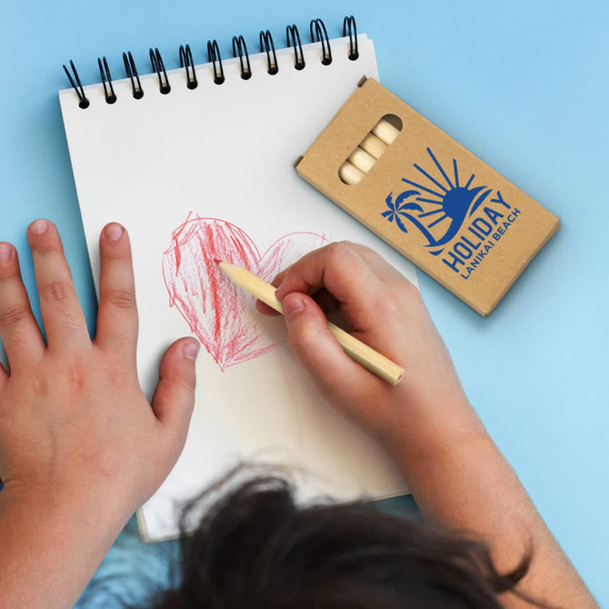 A set of coloured pencils in a cardboard packaging, with a child’s hand drawing a heart shape on a sketchbook page.