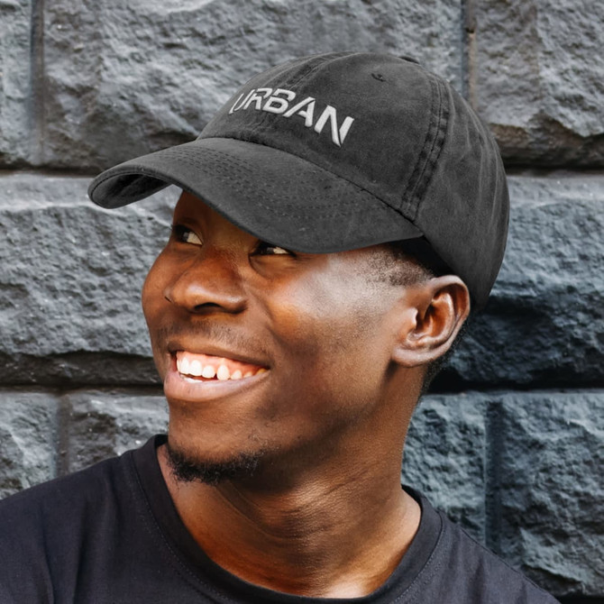 A black cap with a logo, featuring a curved brim, worn by a smiling individual against a textured stone background.