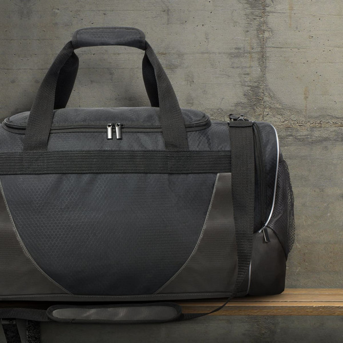 A black duffle bag with grey accents and a logo, featuring handles and a zipper closure, resting on a wooden surface.