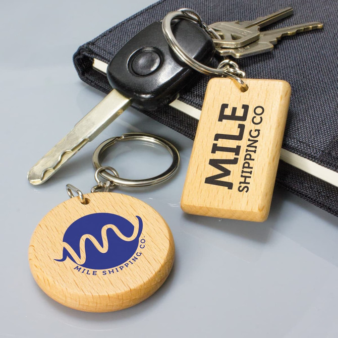 A round wooden key ring in a natural finish, featuring a logo, alongside a rectangular key ring on a keychain.