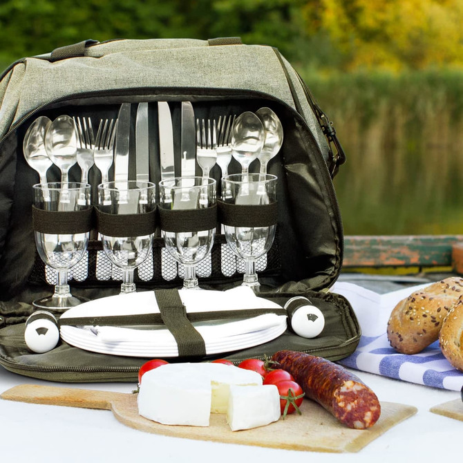 A grey picnic bag with cutlery, glasses, plates, and food items, set against a natural background.