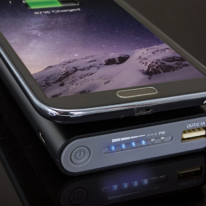 A wireless power bank in black, charging a smartphone, with LED indicators showing battery level.