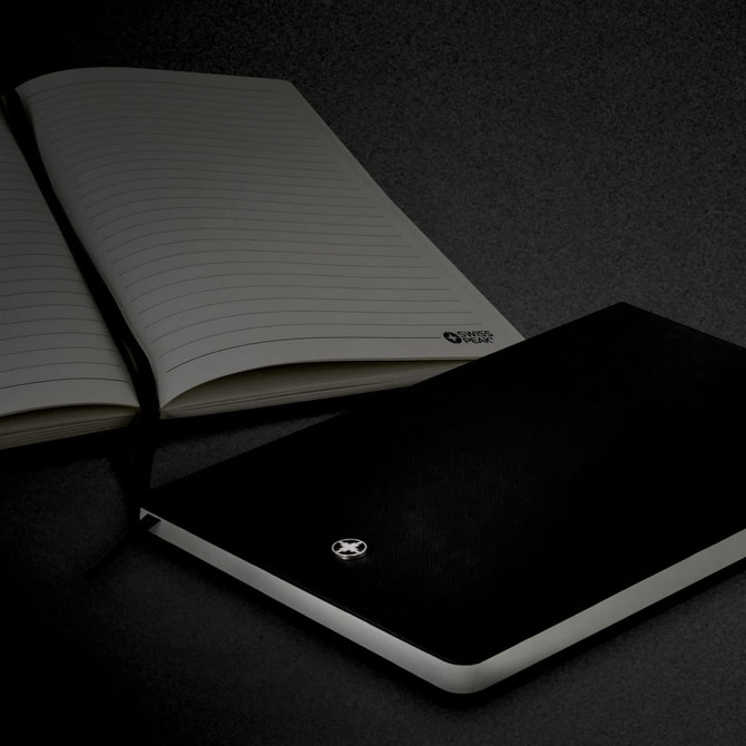 A black A5 notebook with a smooth cover, accompanied by an open lined notebook, featuring a logo.