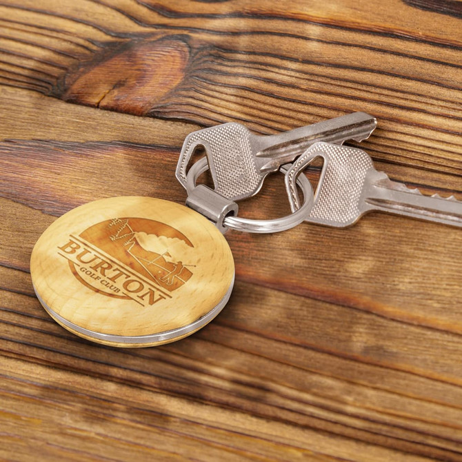 A round wooden key ring featuring a logo, resting alongside metal keys on a wooden surface.