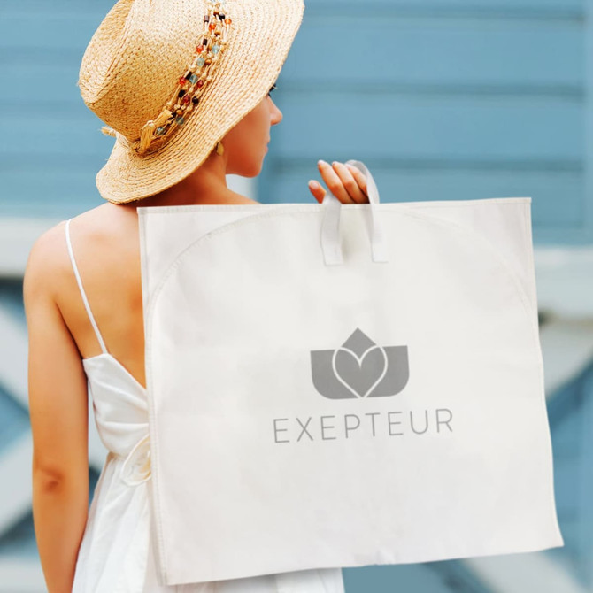 A beige garment bag with handles and a logo, held by a person wearing a straw hat and a white dress.
