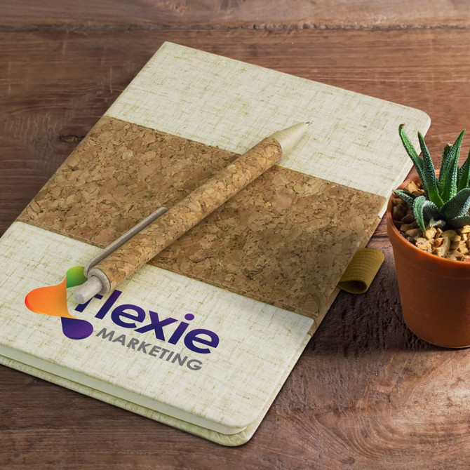 A cork and cream notebook with a matching pen, alongside a small potted plant on a wooden surface.