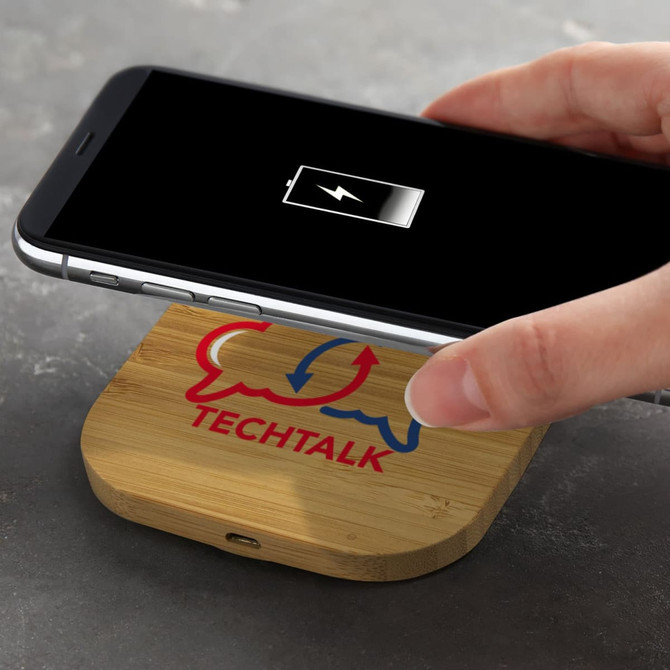 A square bamboo wireless charger with a smartphone placed on it, featuring a logo.
