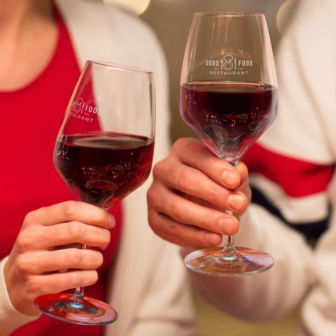 Two elegant wine glasses, each filled with red wine, featuring a logo on the glass. The glasses have a classic shape.