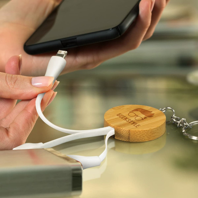 A round bamboo charging cable key ring in white, with a logo, connecting to a smartphone.