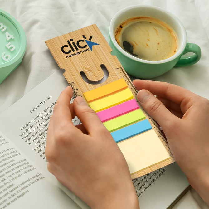 A bamboo ruler bookmark with multicoloured sticky notes, resting next to a cup of coffee and an open book.