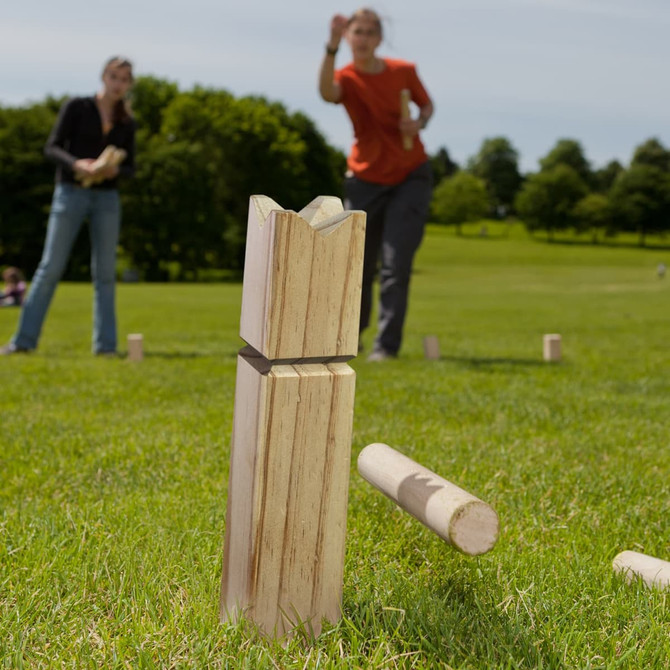 A wooden Kubb game set on grass, featuring light-coloured wooden blocks and a player in the background.