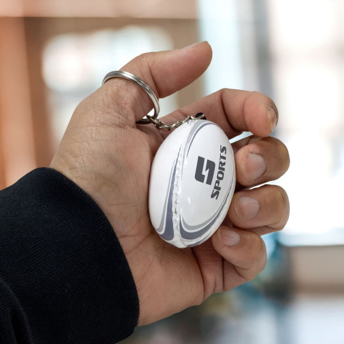 A rugby ball key ring held in a hand, featuring a white design and a logo.