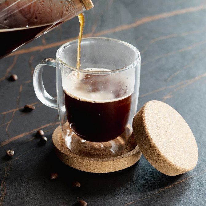 A clear glass coffee cup with a cork base and lid, featuring a stylish handle.