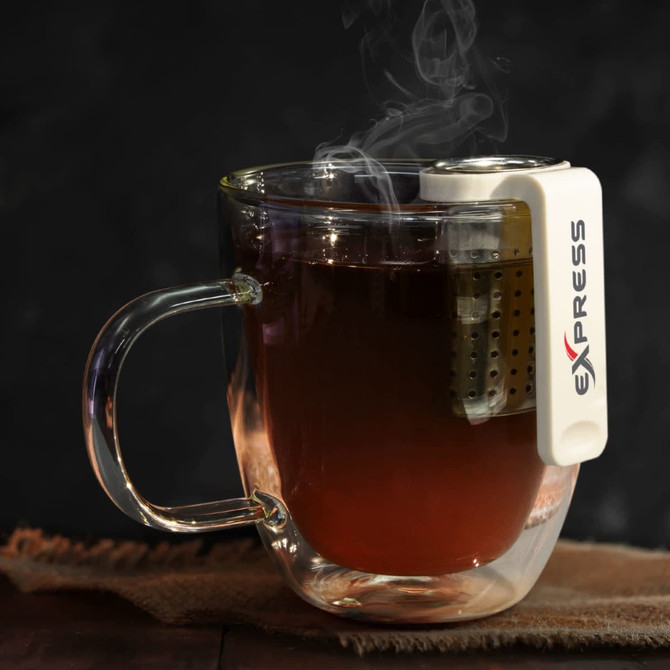 A clear glass mug containing tea, with a white tea infuser attached, emitting steam. The mug has a handle.