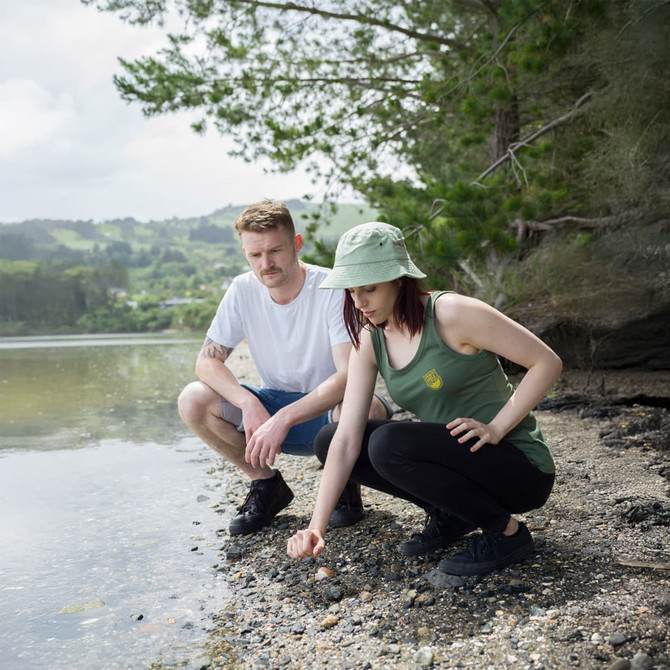 A green tank top is worn by a woman kneeling on the shore, while a man sits beside her. Both are outdoors.