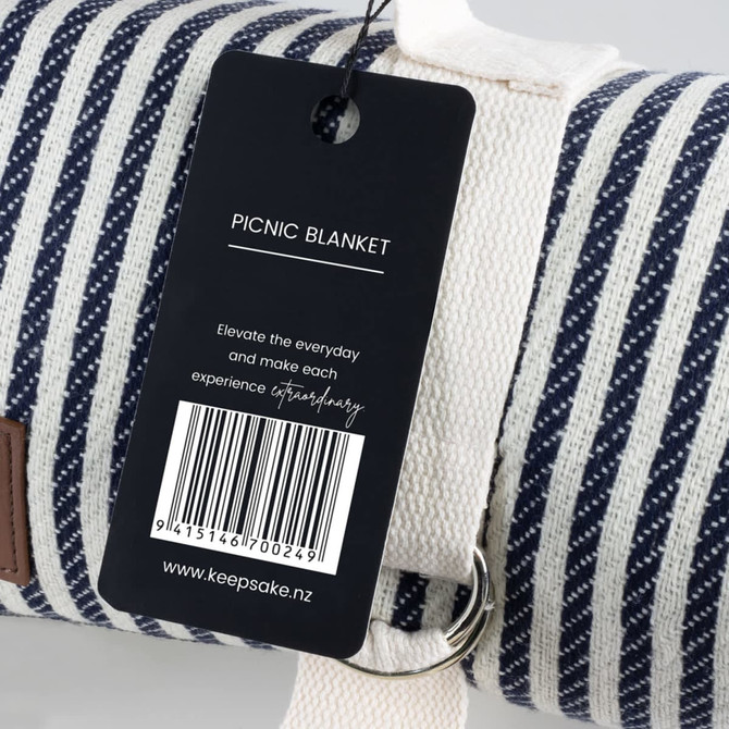 A striped picnic blanket in blue and white with a branded tag and a metal loop for easy carrying.