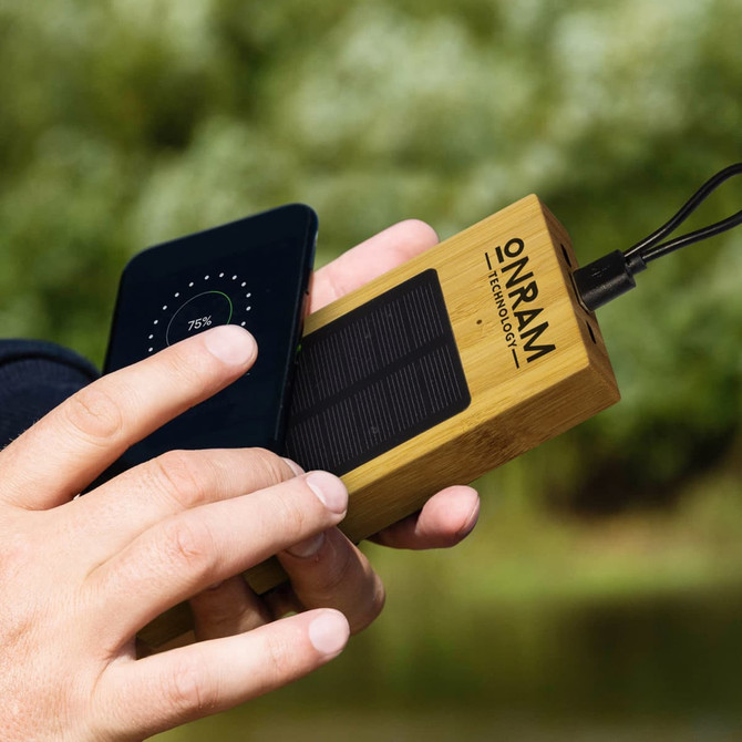 A bamboo solar power bank in a hand, connecting to a smartphone, featuring a black solar panel and branding.