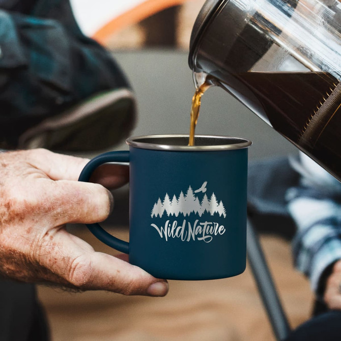 A drinkware mug in navy blue with a nature-themed design and a logo, being filled with coffee.