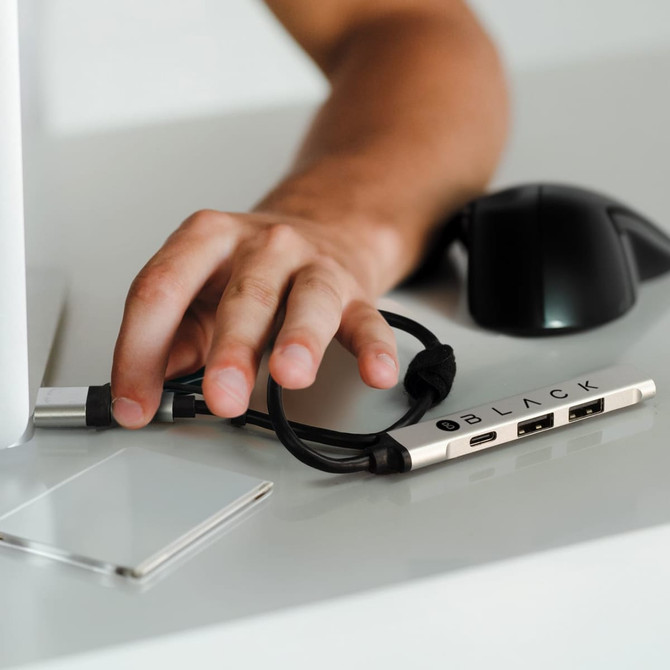 A silver USB hub with multiple ports and a black cable, placed on a desk beside a computer and a mouse.