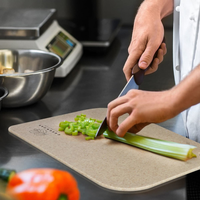 A chopping board in a neutral colour with celery being chopped, featuring a person's hand and a knife.
