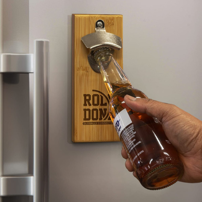 A drink bottle opener made of bamboo with a silver metal cap remover, mounted on a fridge.