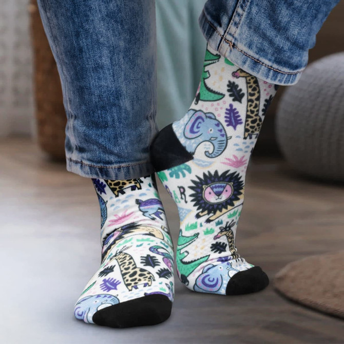 Colourful crew socks featuring playful animal patterns, with a black toe and heel, worn by a person in denim jeans.