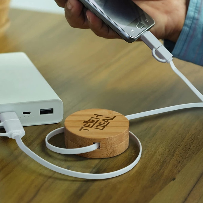 A bamboo retractable charging cable with white cords connected to a phone and portable charger on a wooden surface.