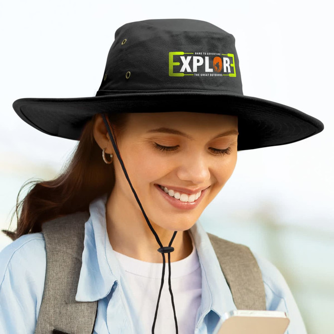 A wide-brim black hat with a logo, featuring a chin strap, worn by a person smiling while holding a phone.