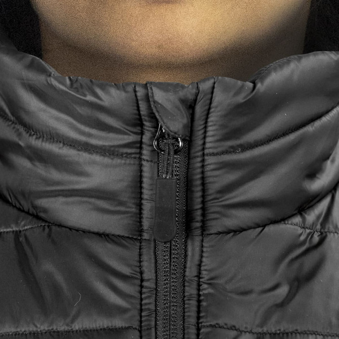 A close-up of a black puffer vest featuring a zippered collar and a logo on the zipper.