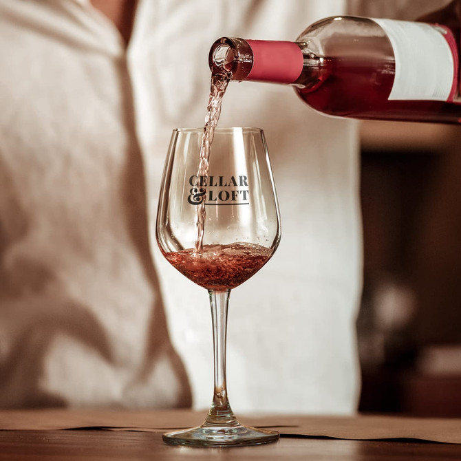 A wine glass with a logo, being filled with pink wine, showcasing its elegant shape and clear glass.