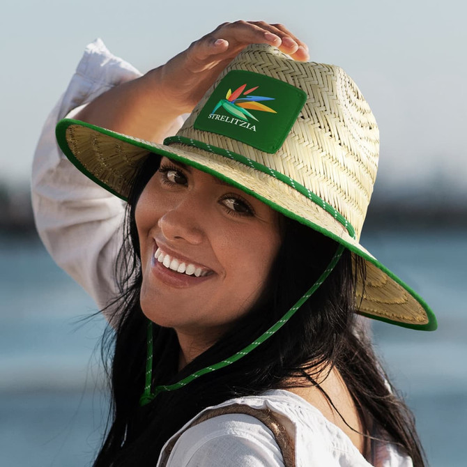 A straw Tiki hat in natural tones with a green band and logo, worn by a smiling woman.