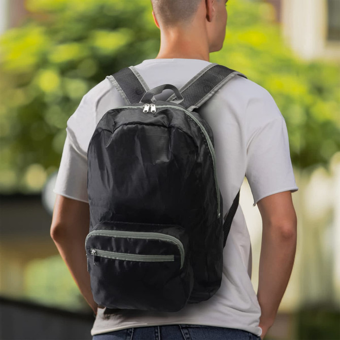 A black foldable backpack with green accents is worn by a person, set against a blurred outdoor background.