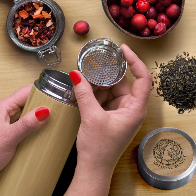 A drink bottle in bamboo with a detachable lid and strainer, surrounded by dried fruits and tea leaves.